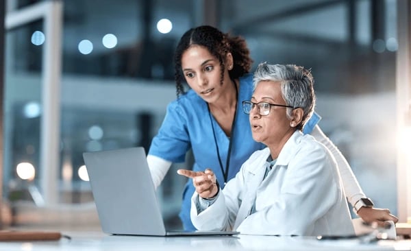 Two female scientists in lab coats examining data on a tablet